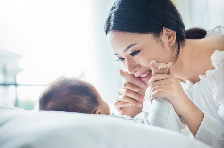 A new mum smiles down at her baby who has its hands on either side of its Mum's face