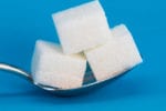 A silver spoon balancing three white cubes of sugar is set against a blue background