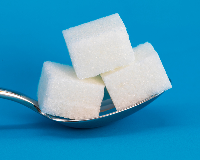 A silver spoon balancing three white cubes of sugar is set against a blue background