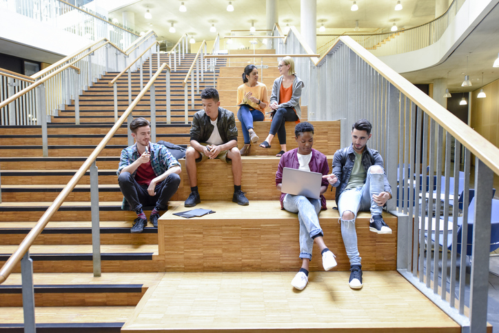 University students sit on stairs with laptops looking happ