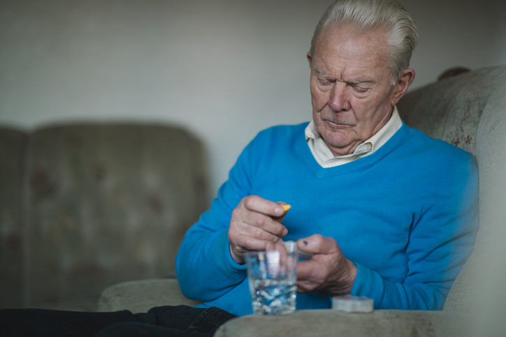 An elderly man sits on the sofa and organises his pills