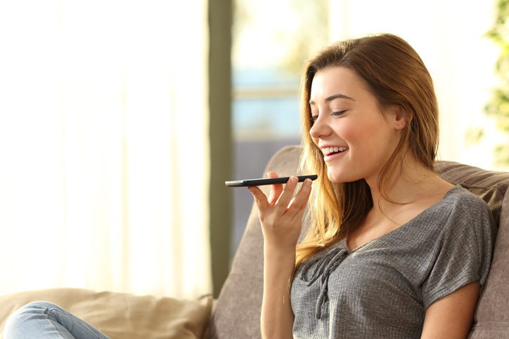 A woman sits on a sofa and speaks into her phone