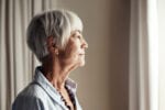 An elderly woman looks out of a window